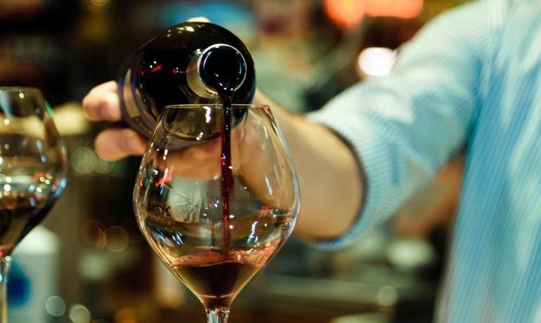 Verso di vino rosso in calice, atmosfera calda e conviviale.