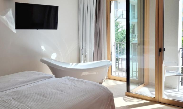 Bright room with a bathtub, bed, and sunny balcony.