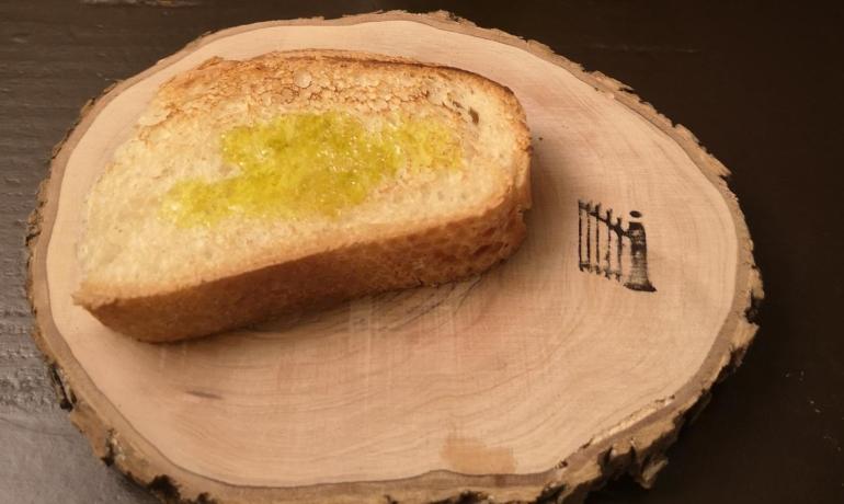 Slice of bread with green oil on rustic board, green bottle beside.