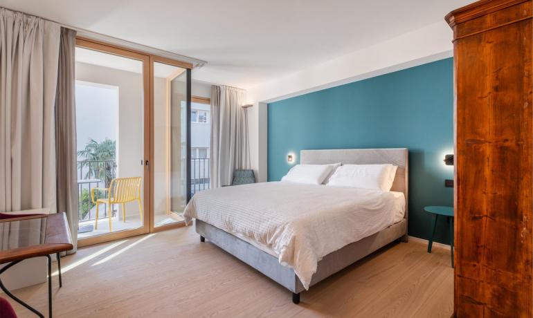 Bright room with cozy bed, blue wall, and balcony with yellow chair.