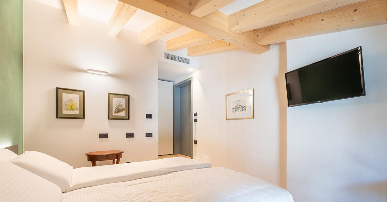 Camera accogliente con letto bianco, travi in legno e TV.