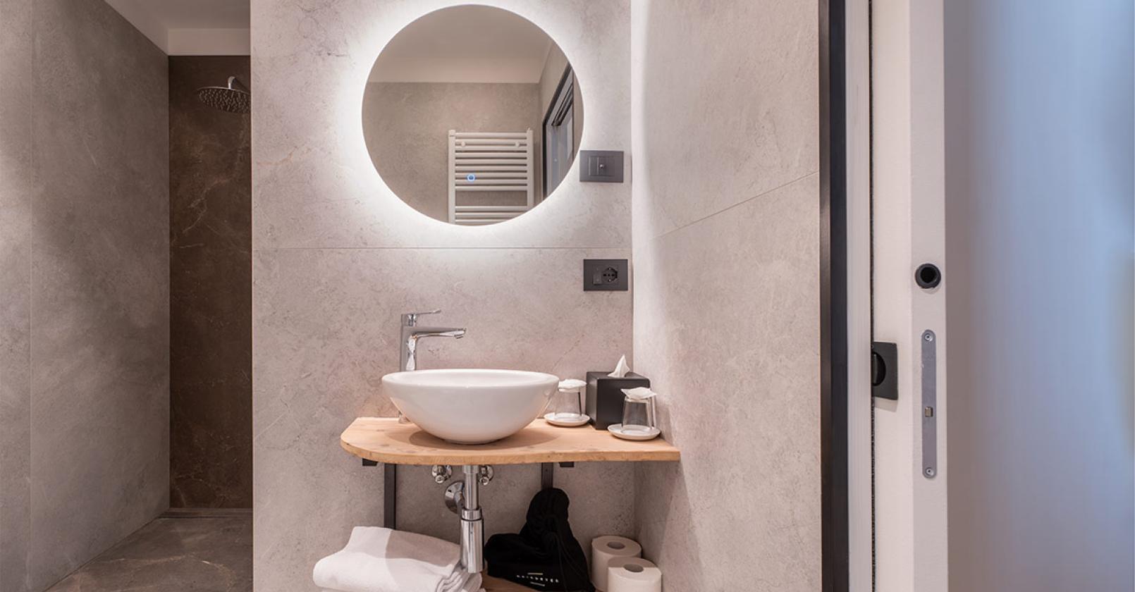 Bagno moderno, elegante, con specchio illuminato e lavandino su mensola in legno.