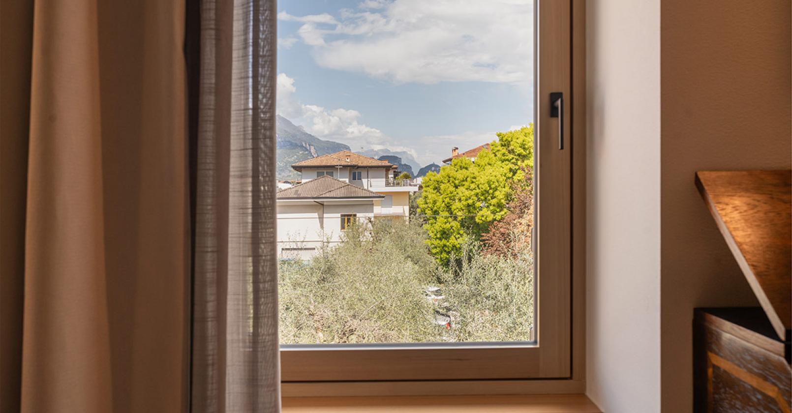 Vista serena dalla finestra su case, montagne e alberi verdi.