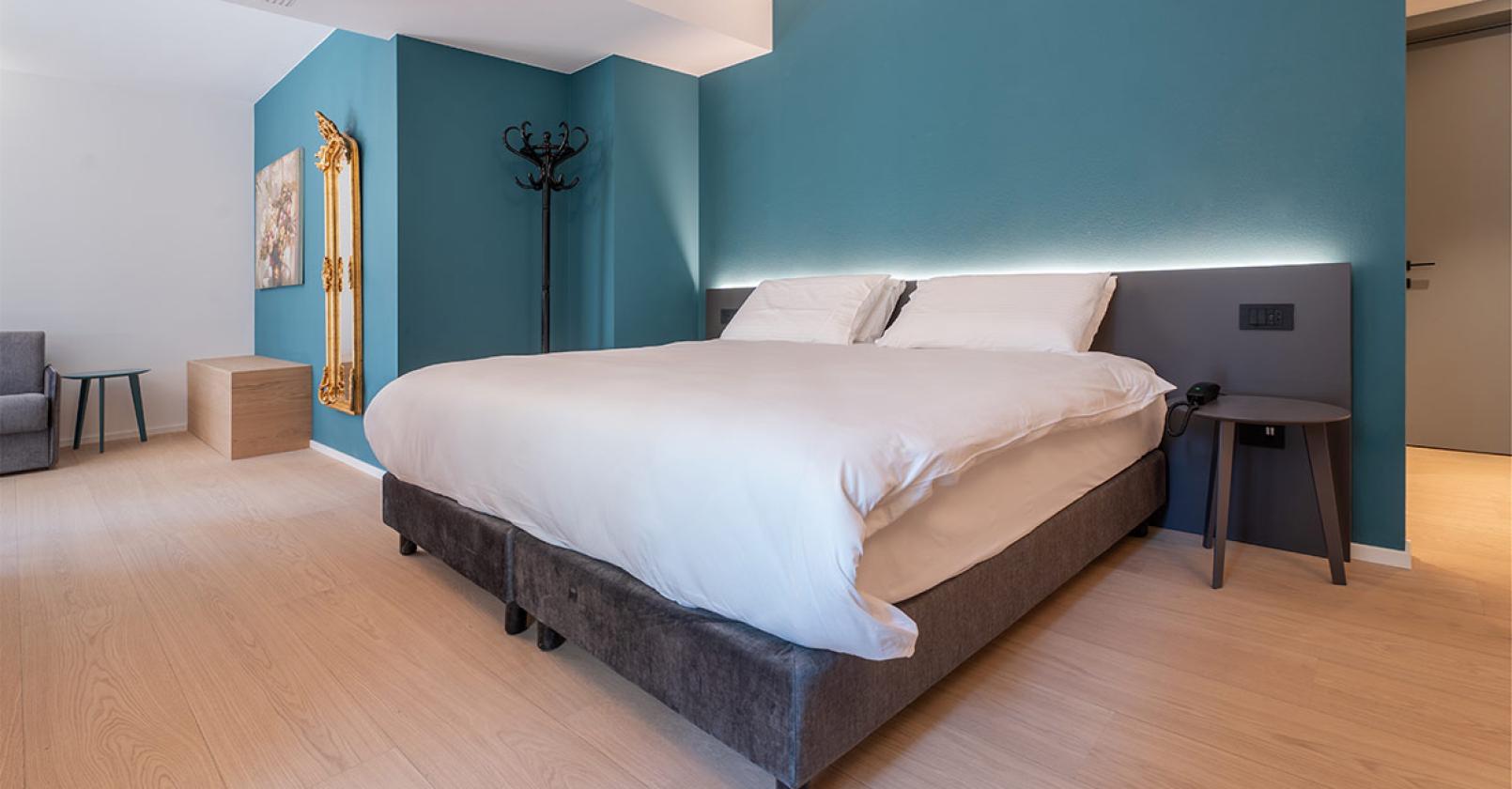 Camera moderna e accogliente, letto comodo, pareti blu rilassanti, atmosfera elegante.