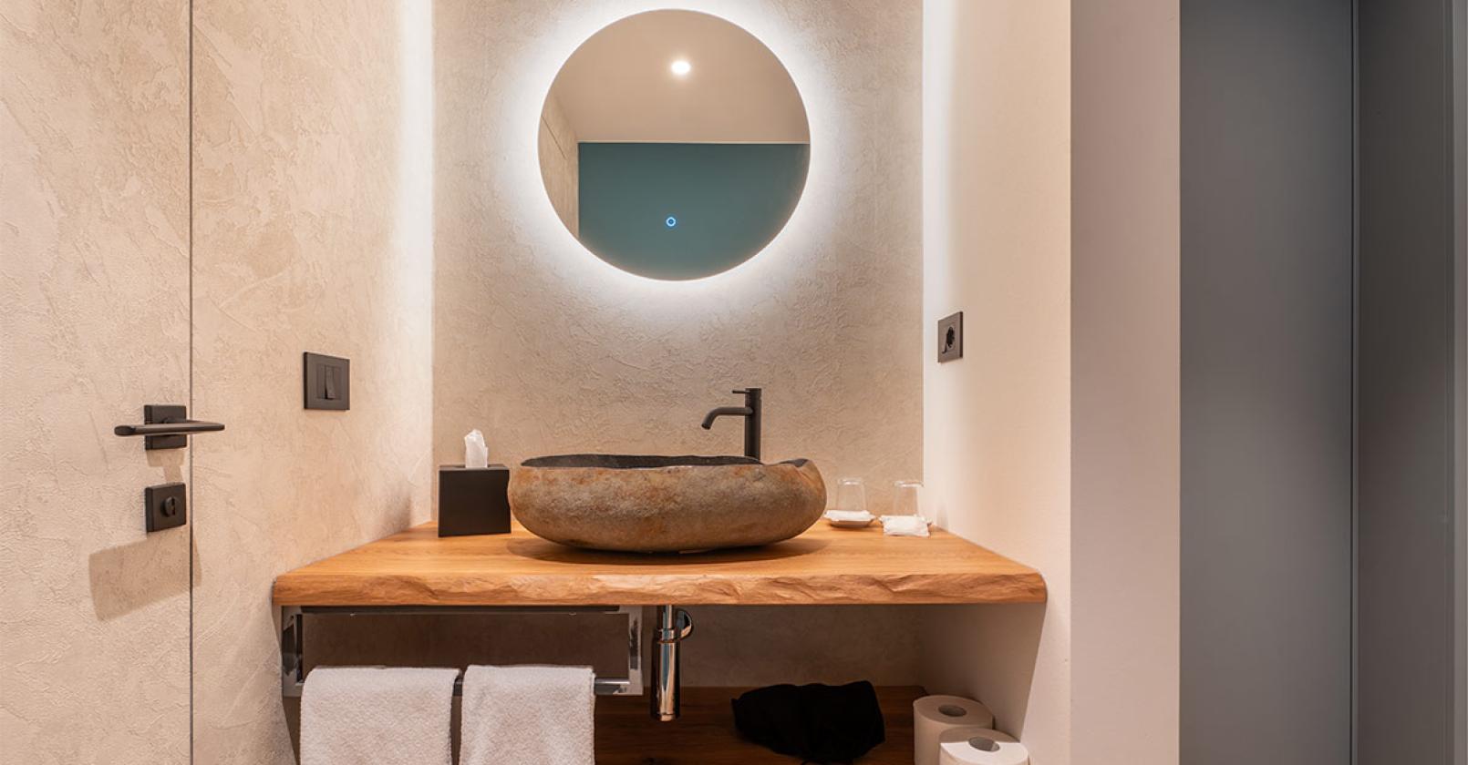 Bagno moderno con lavabo in pietra e specchio illuminato, atmosfera calda e accogliente.