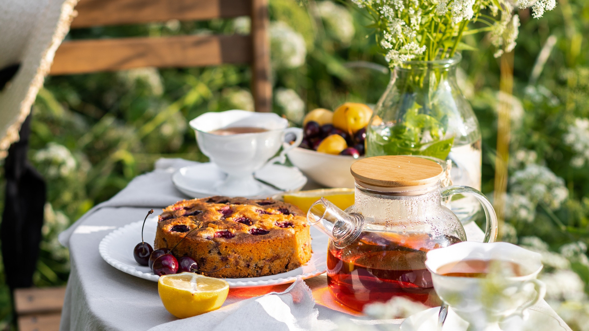 Gartentisch mit Tee, Kuchen und frischen Blumen.