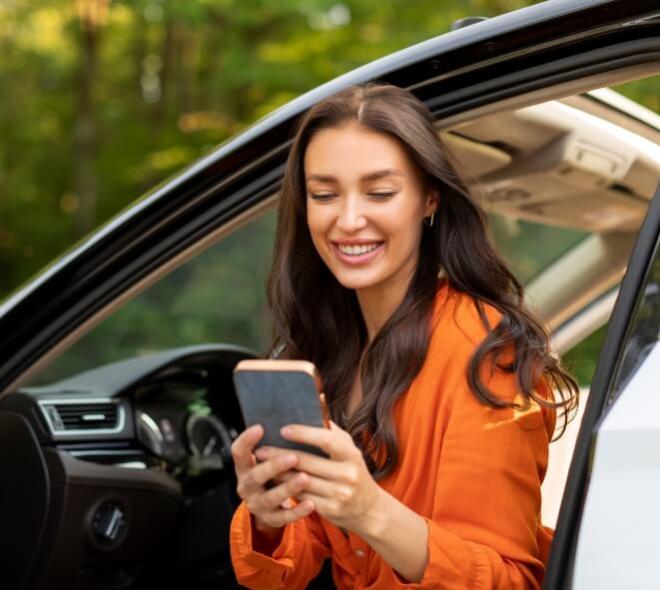 Donna sorridente in auto guarda il cellulare, atmosfera serena e felice.