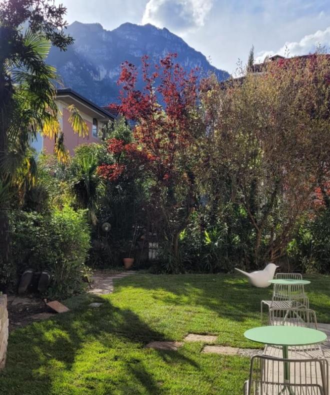 Giardino verde, tavolini, montagne sullo sfondo, atmosfera serena e luminosa.